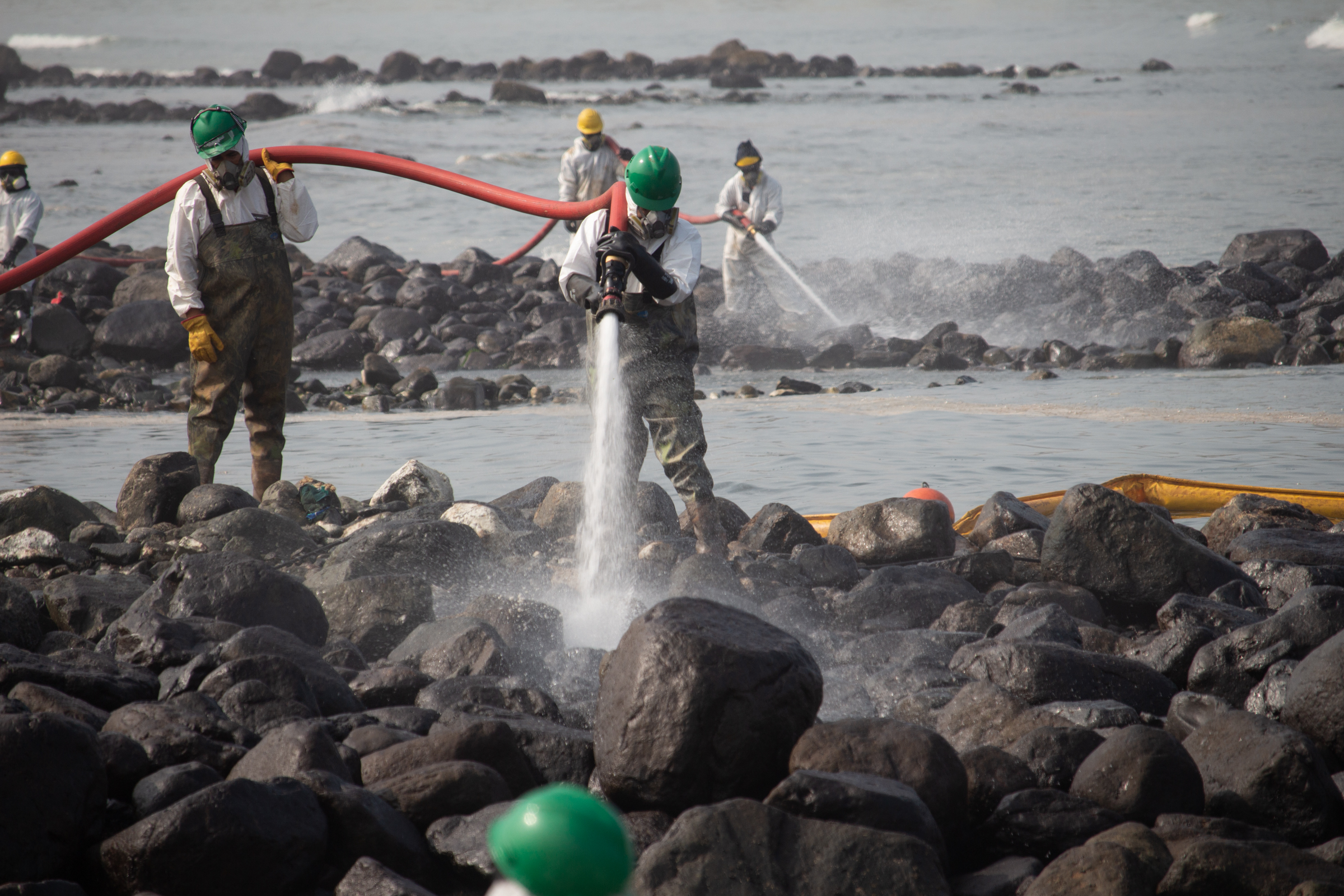 People spraying water from hoses to wash off crude oil